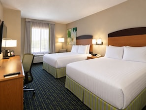 Une chambre d’hôtel avec deux lits, un bureau, une chaise, une lampe, un téléphone et un tableau au mur.