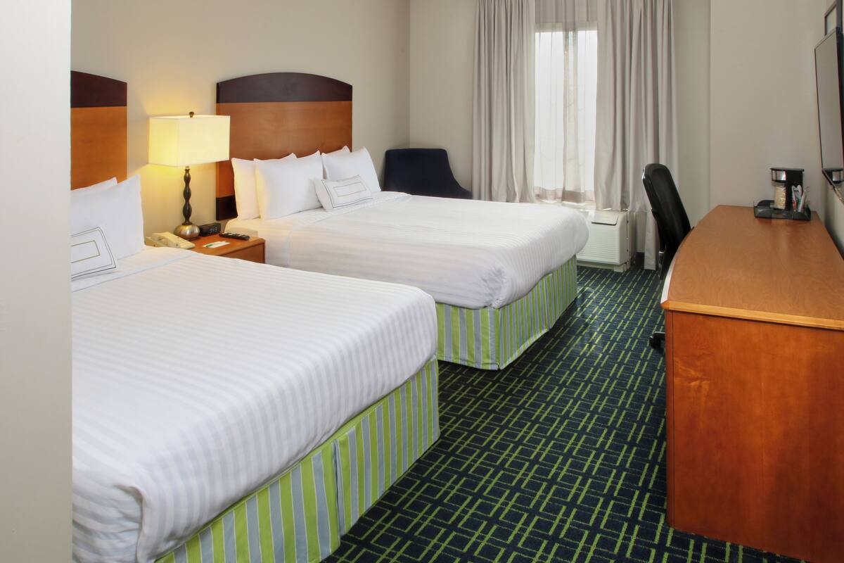 Habitación de hotel con dos camas, un escritorio, una silla, una lámpara y una ventana con cortinas.
