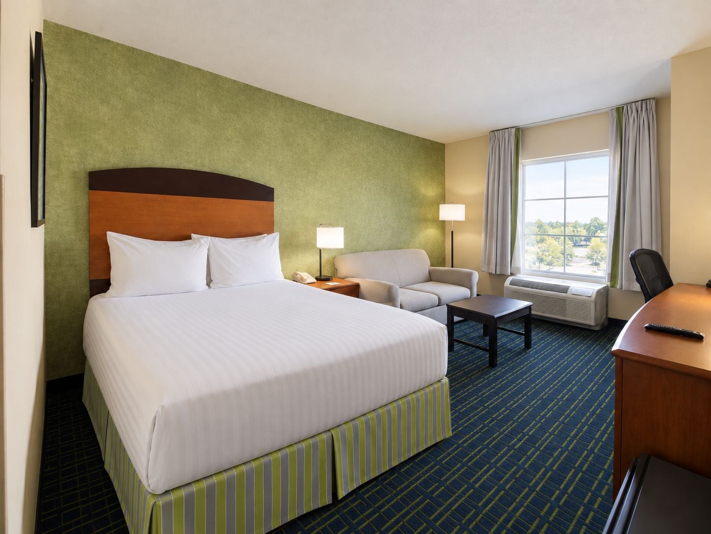 A hotel room with a large bed, a desk, a chair, a sofa, and a window with curtains.