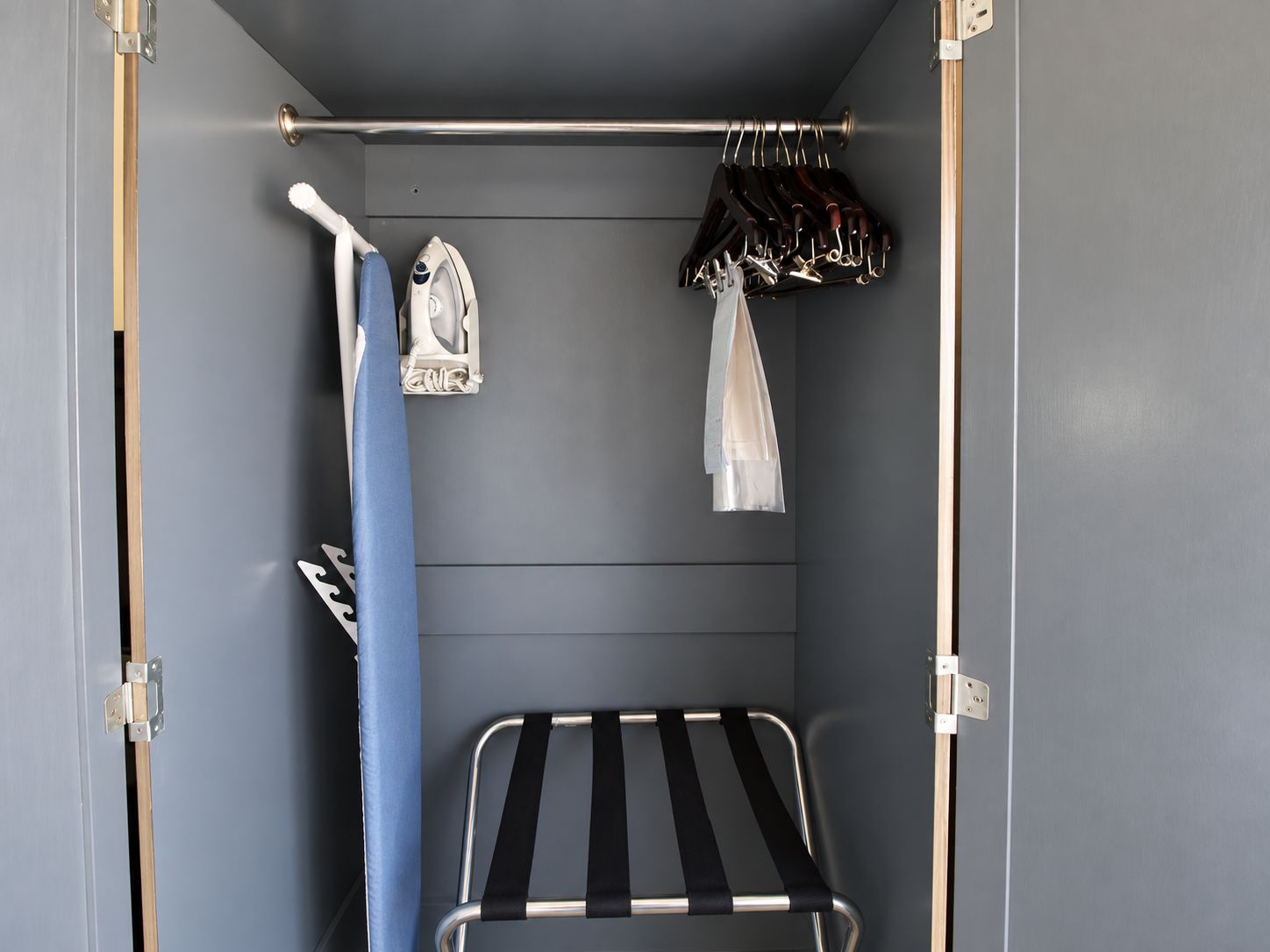 A compact room with a metal rack for hanging clothes, a small ironing board, and a towel rack.