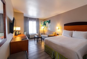 Una habitación de hotel con cama, escritorio, silla y un cuadro en la pared.