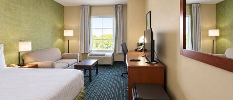 A hotel room with a bed, a desk, a chair, a small refrigerator, and a window with curtains.