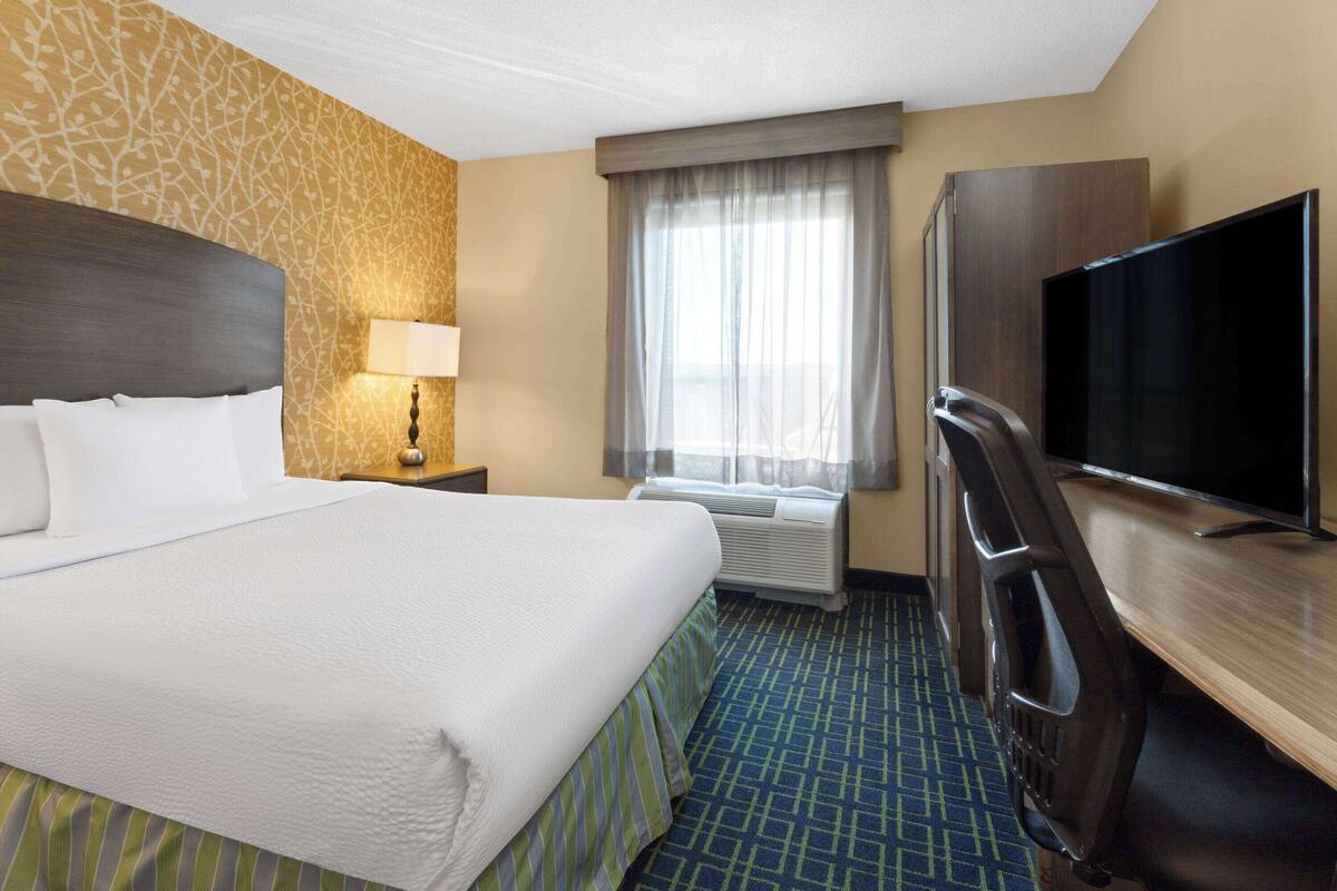 Habitación de hotel con una cama grande, un escritorio con televisor de pantalla plana, una lámpara y una ventana con cortinas.