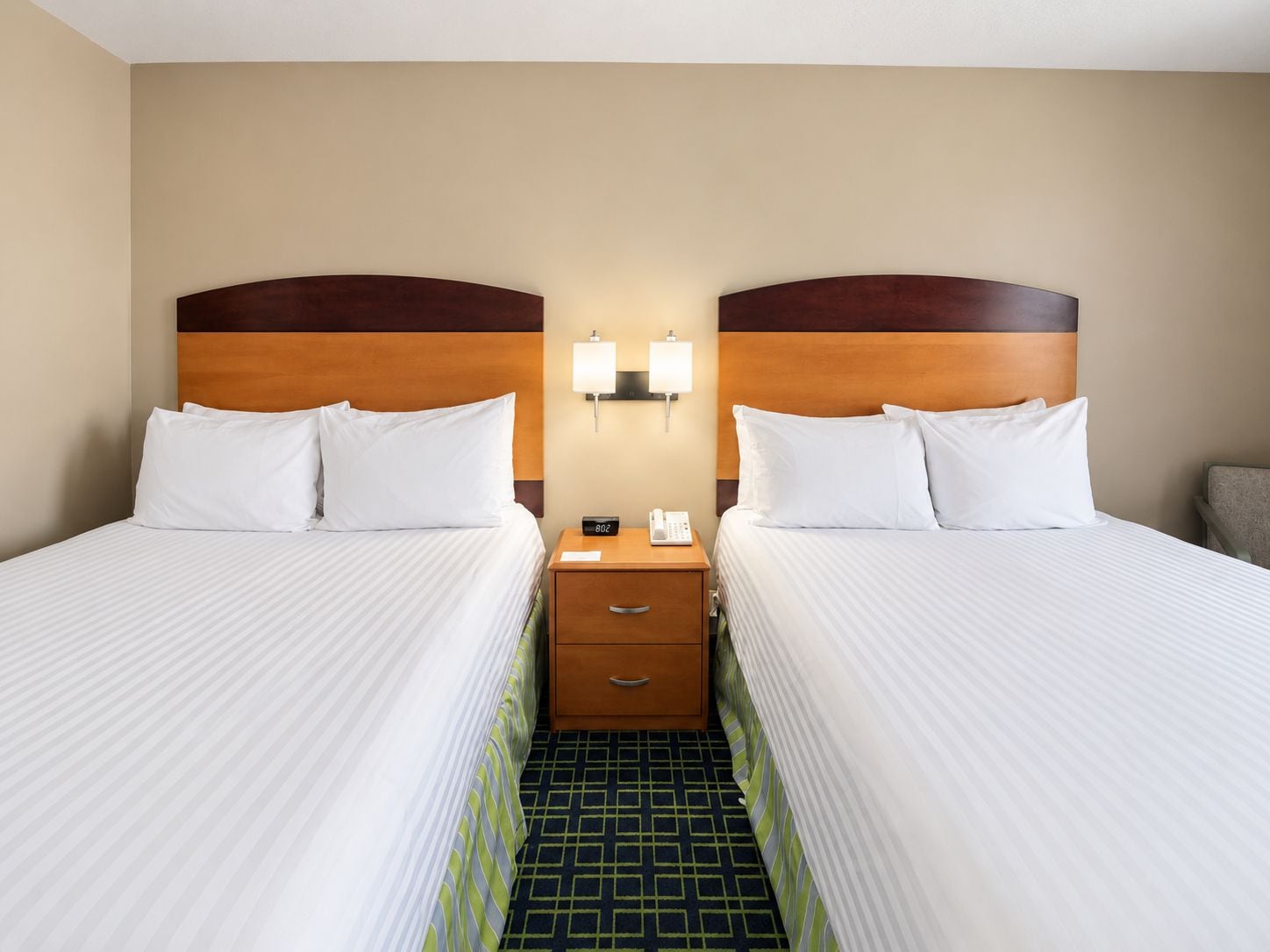 Habitación de hotel con dos camas, una mesita de noche con teléfono y una lámpara de pared.