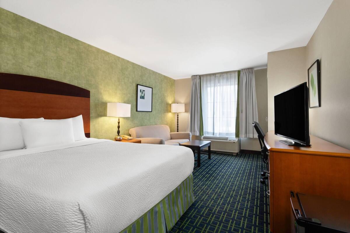 Habitación de hotel con una cama grande, un escritorio con televisor, una silla y una lámpara de escritorio.