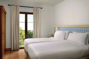 Una habitación de hotel con dos camas, una ventana con cortinas, un armario de madera y una mesita de noche con lámpara.