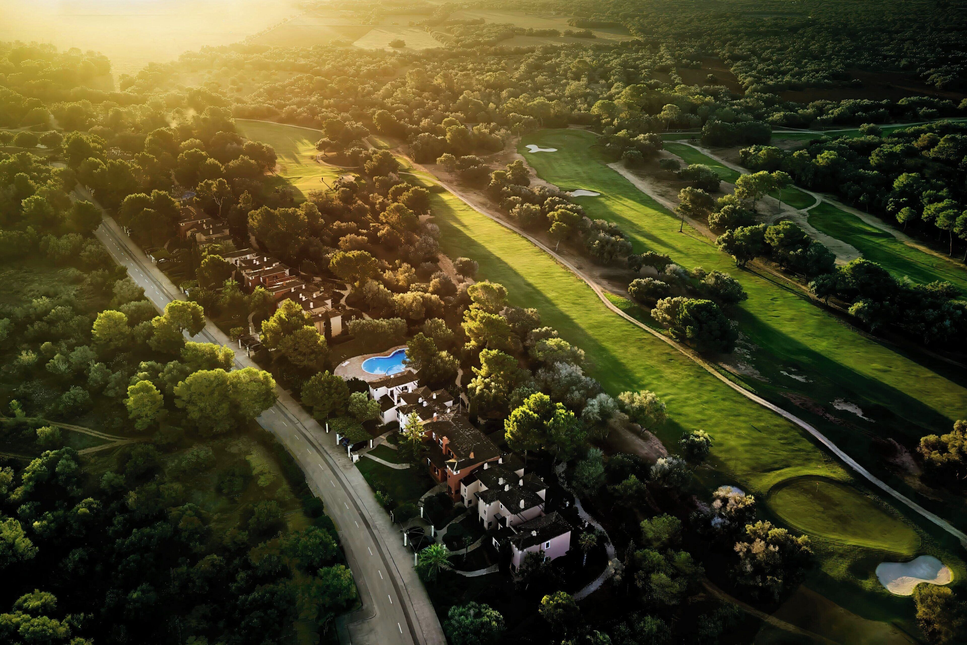 Luchtbeeld van een golfbaan met een clubhuis, meerdere greens en een zwembad.