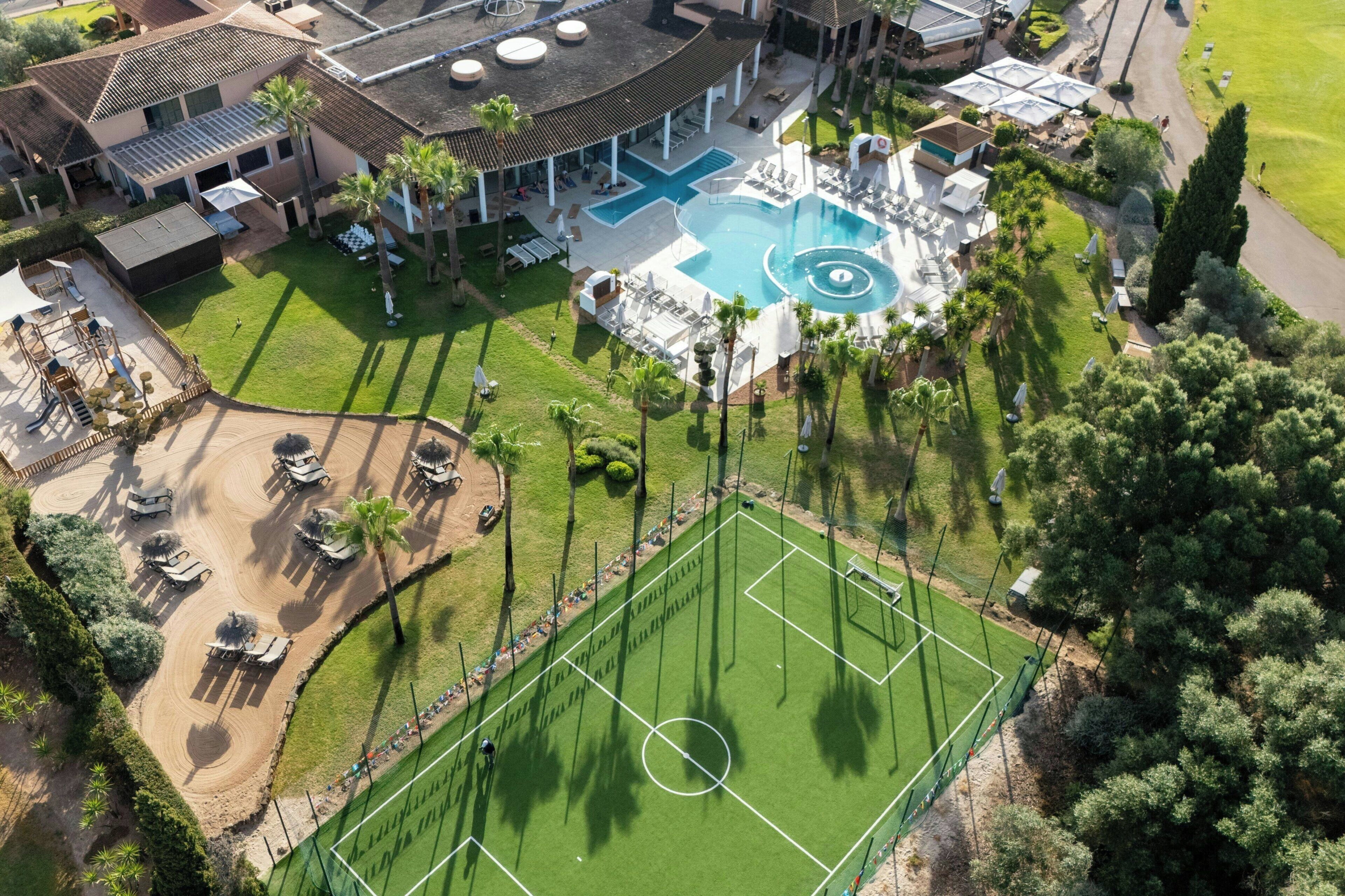 Vista aerea di un resort con piscina, lettini e campo da tennis.