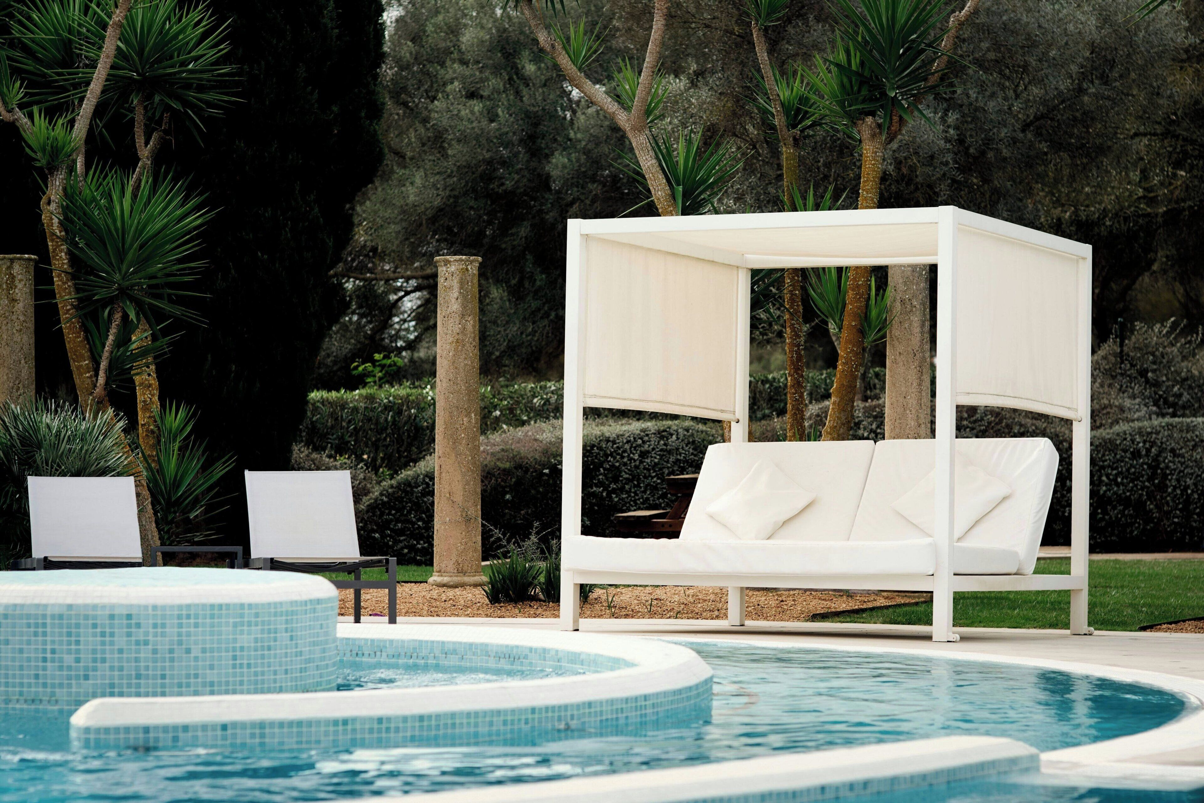 A poolside area with a white canopy bed, lounge chairs, and a tiled pool.
