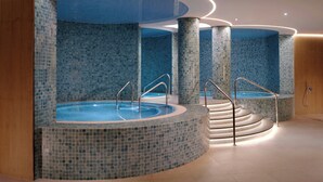 Een moderne spa-ruimte met een rond bubbelbad, betegelde muren en een trap naar een hoger niveau.
