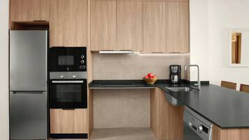 A modern kitchen with wooden cabinets, a stainless steel refrigerator, an oven, a dishwasher, and a black countertop.