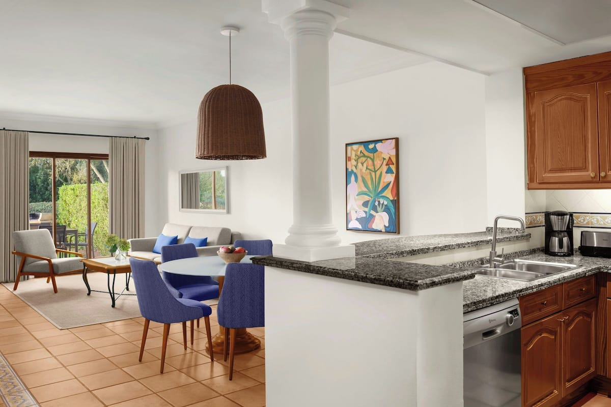 Una cocina moderna con encimera de granito, armarios blancos y un comedor con sillas azules y una mesa redonda.