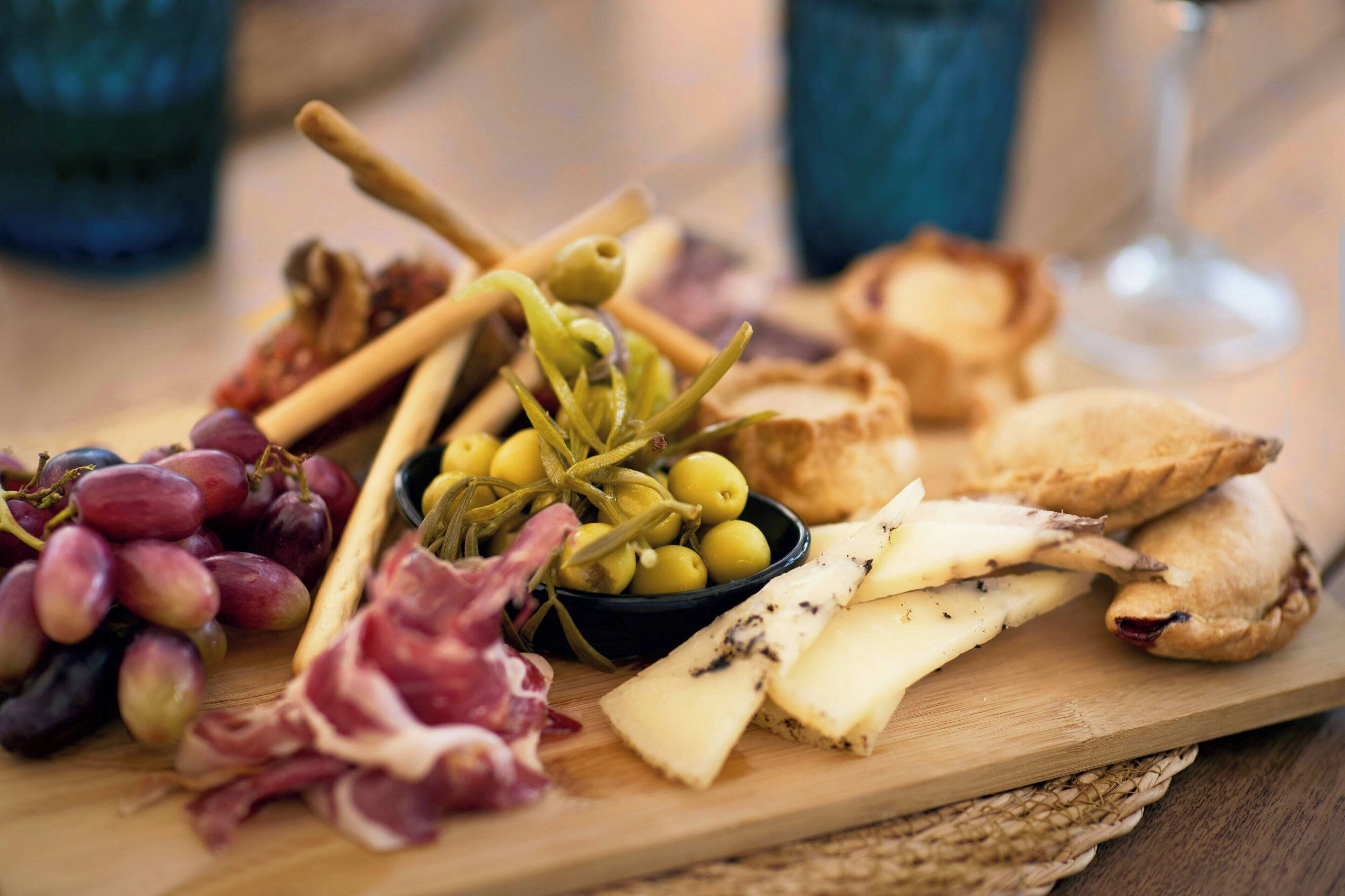 Una tabla de madera con varios quesos, uvas, aceitunas y galletas.