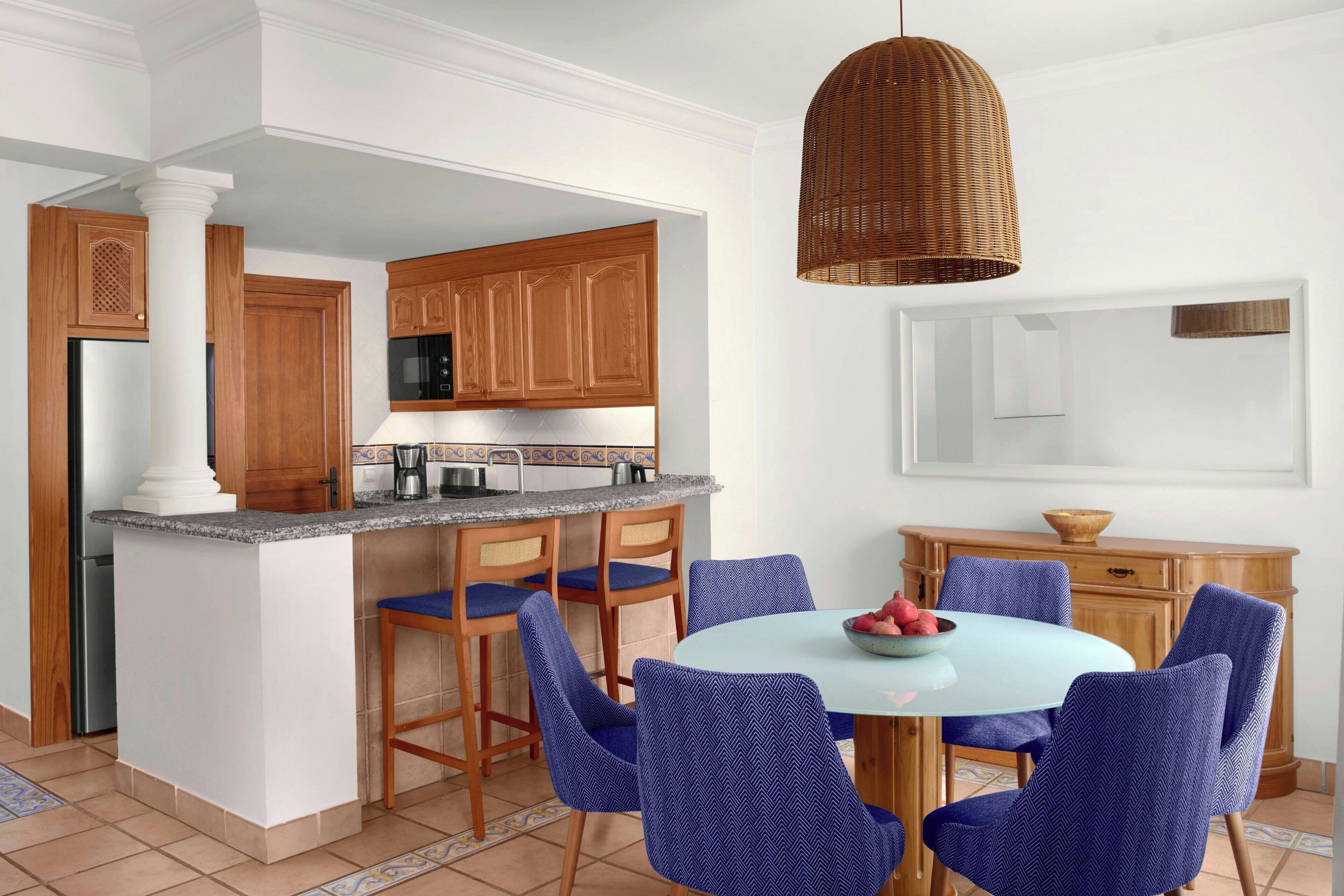 Una cocina moderna con armarios de madera, un refrigerador de acero inoxidable y una mesa de comedor redonda con sillas azules.