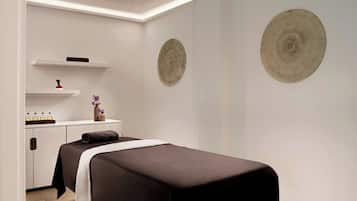 A modern spa room with a massage table, shelves with bottles, and two circular wall decorations.