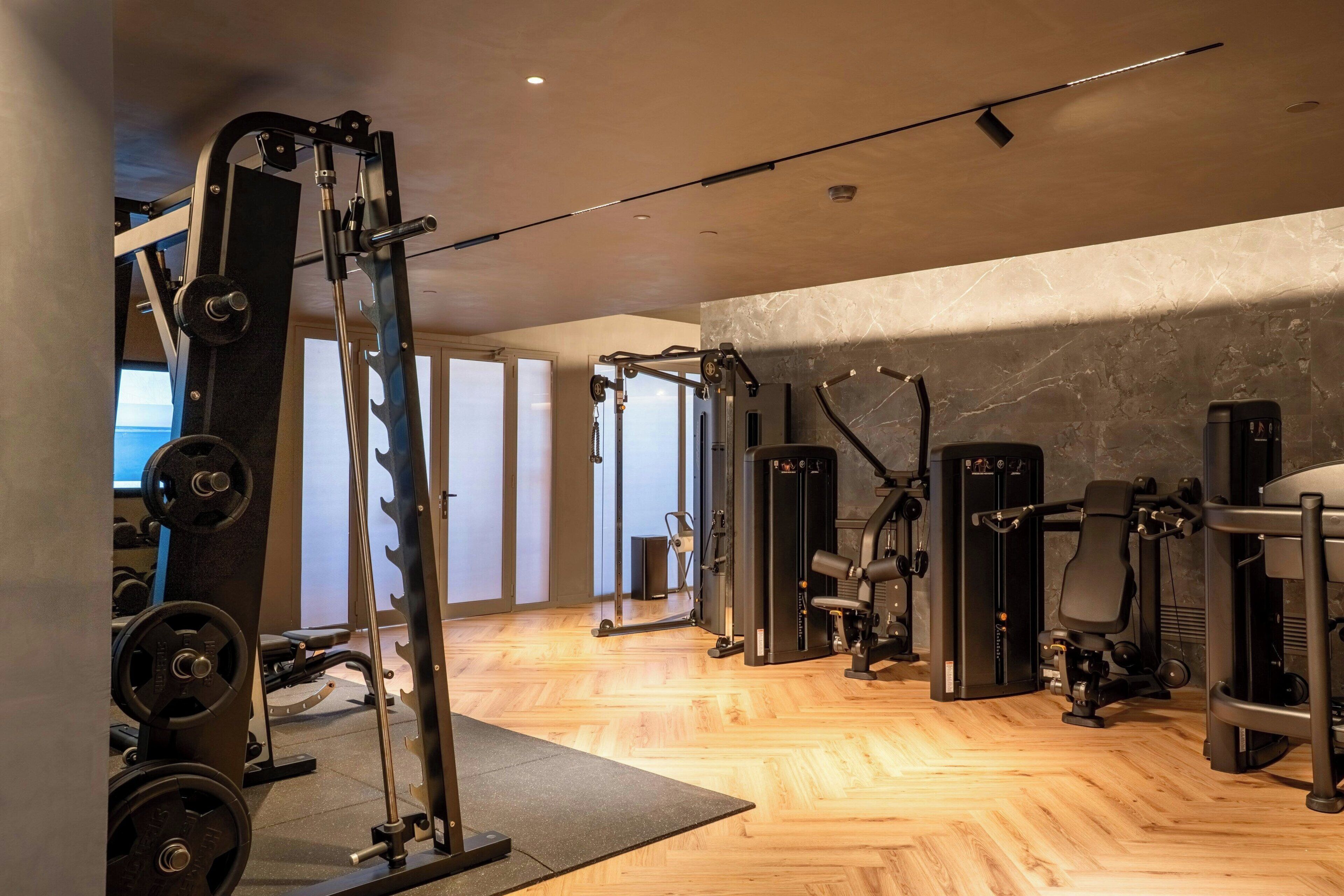 Une salle de sport équipée de divers appareils d’exercice, dotée d’un plancher en bois et d’une grande fenêtre.