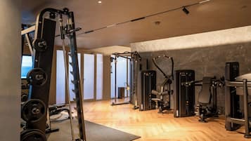 Een sportschool met diverse fitnessapparaten, houten vloeren en een groot raam.