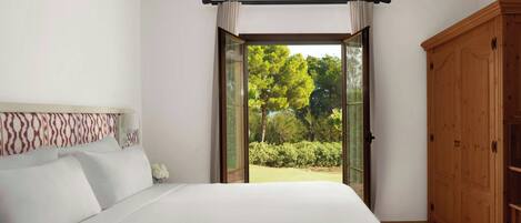 A bedroom with a large bed, a wooden wardrobe, and a view of a garden through an open door.
