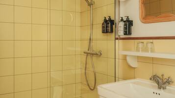 Une salle de bain avec des carreaux jaunes, une douche, un lavabo et un miroir.