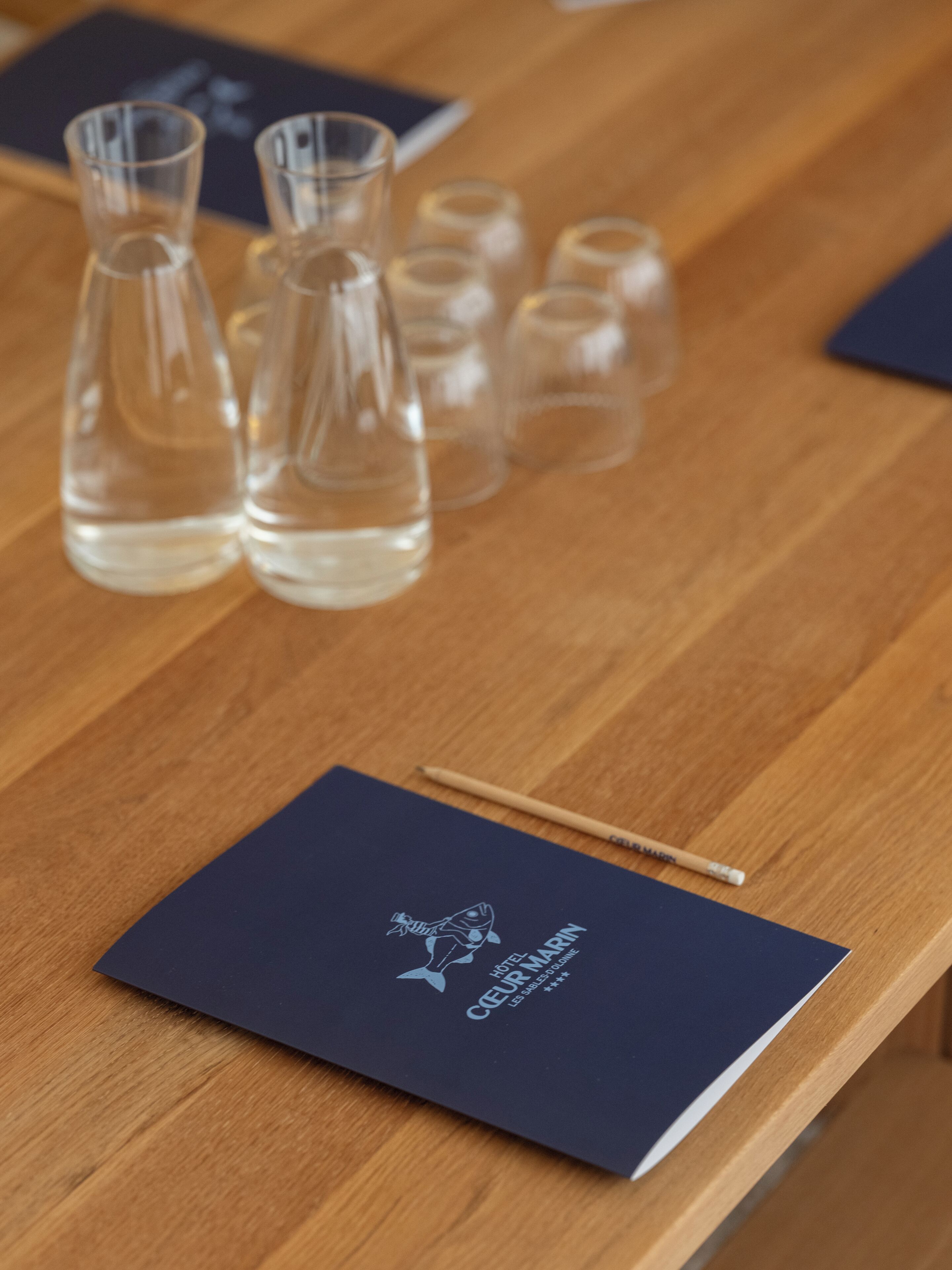 Una mesa de madera con varios jarrones de vidrio transparente y un folleto azul oscuro con un logotipo de pez y texto.