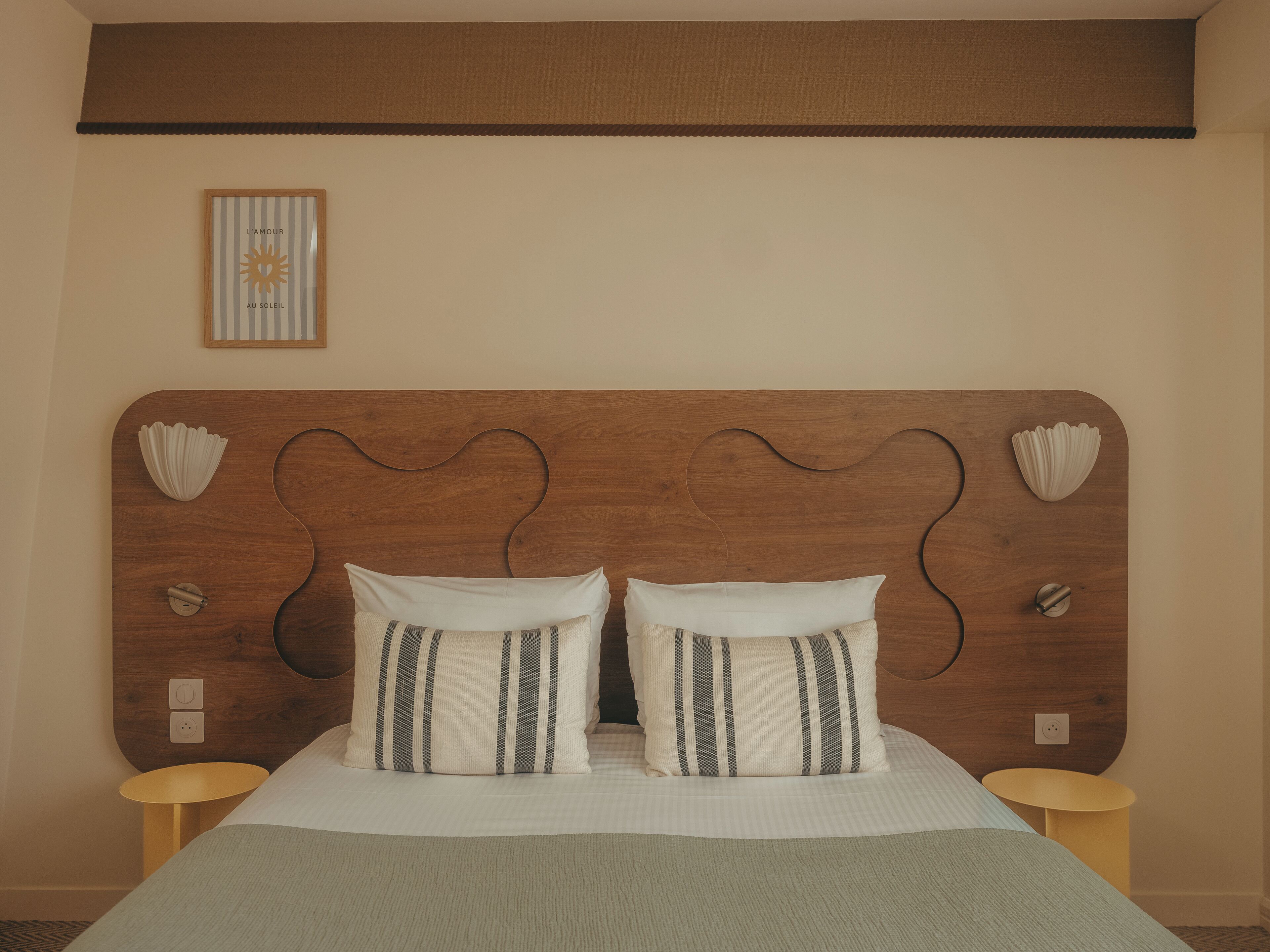 Una cama con cabecera de madera, dos almohadas, dos mesitas de noche y un cuadro en la pared.