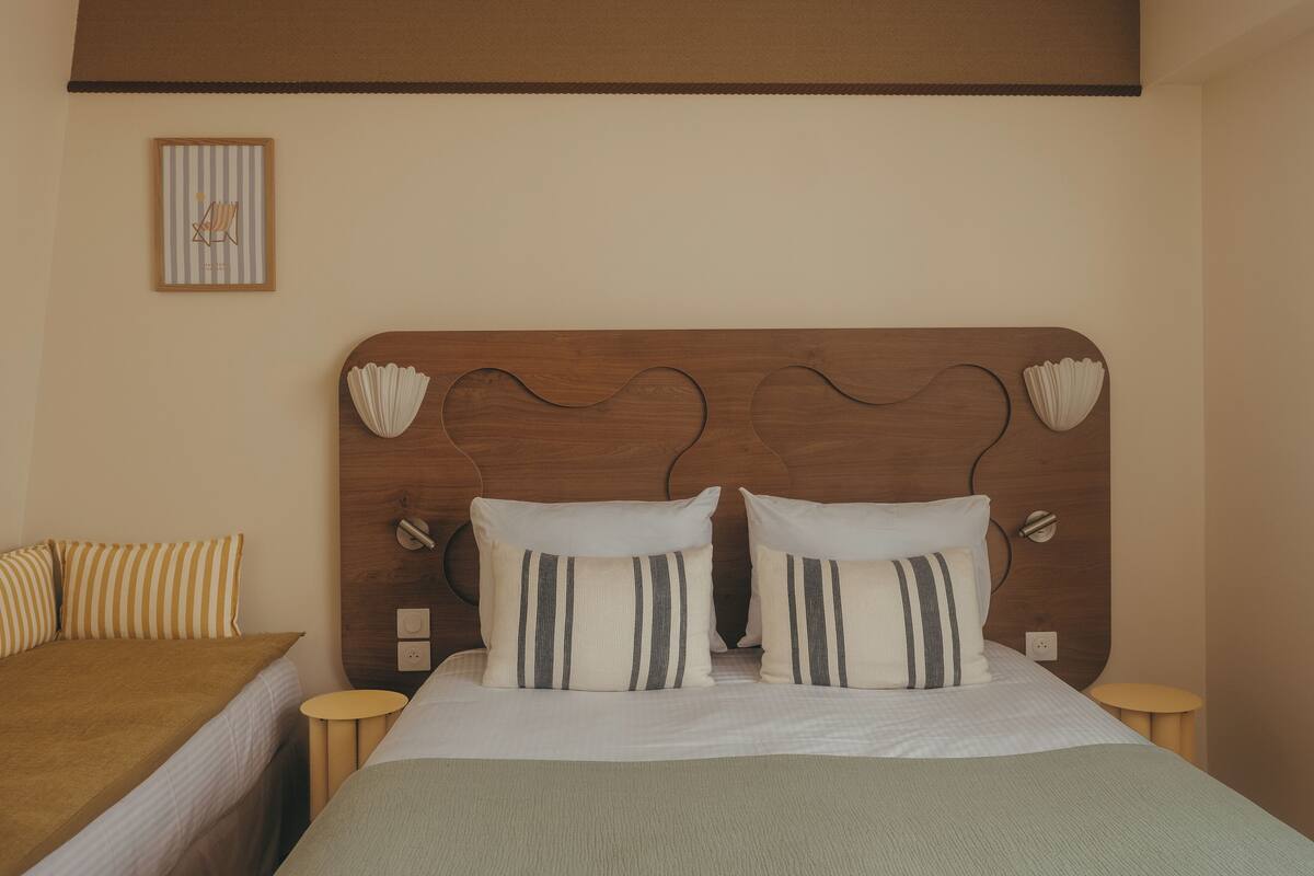 A neatly arranged bedroom with a wooden headboard, two bedside tables, a bed with striped pillows, and a small framed picture on the wall.