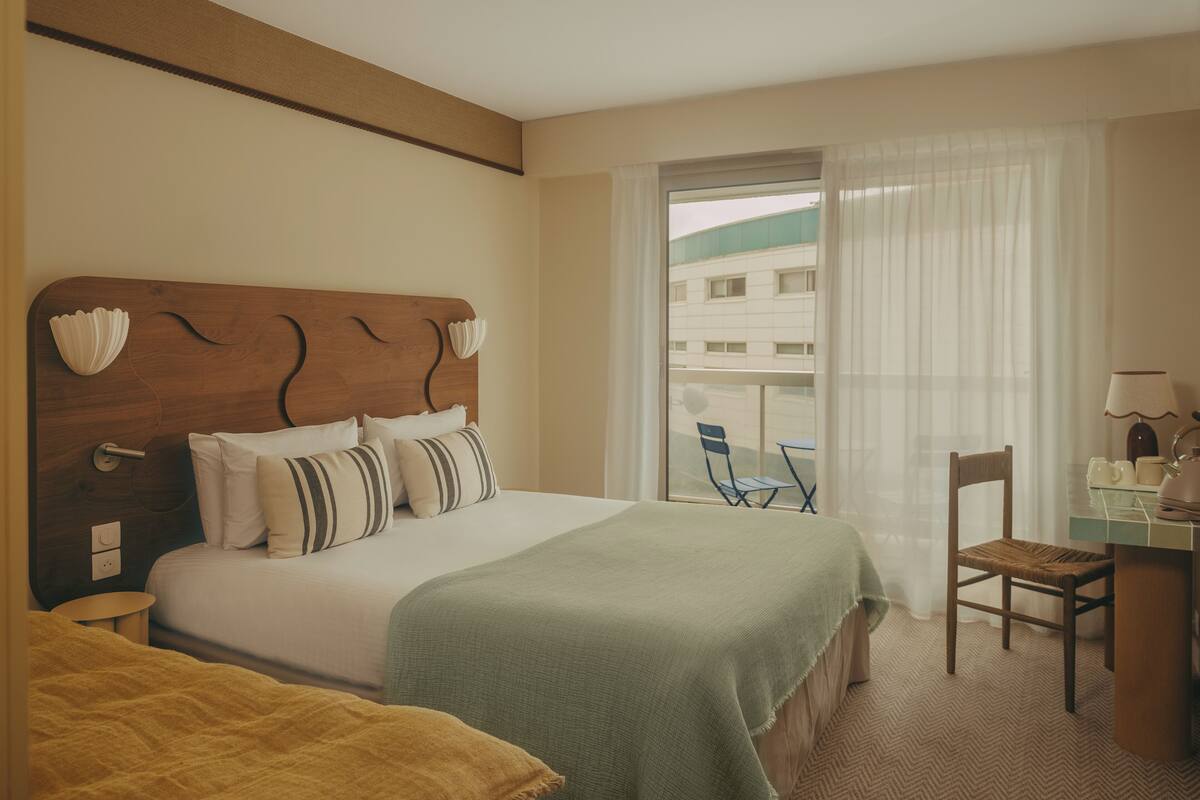 A hotel room with a bed, a desk, a chair, and a view of the outside.