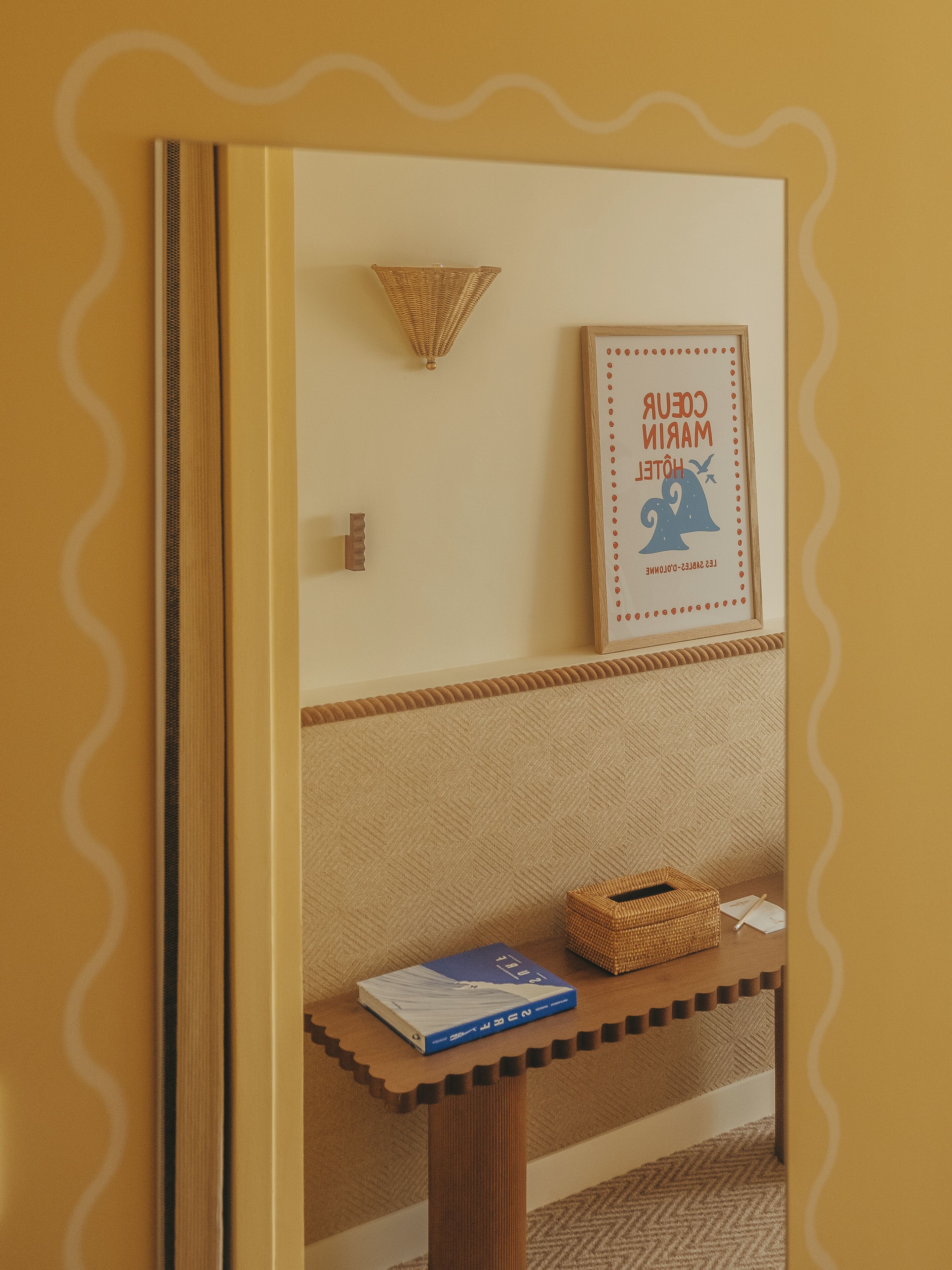 A framed picture of a hotel with a geometric wall pattern and a woven basket on a wooden table.
