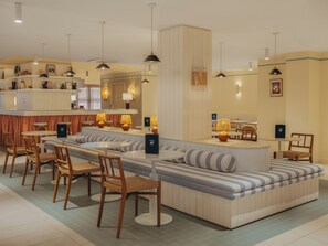 A modern hotel lobby with a central seating area, multiple dining tables, and hanging pendant lights. - Hôtel Coeur Marin (Les Sables-d'Olonne)