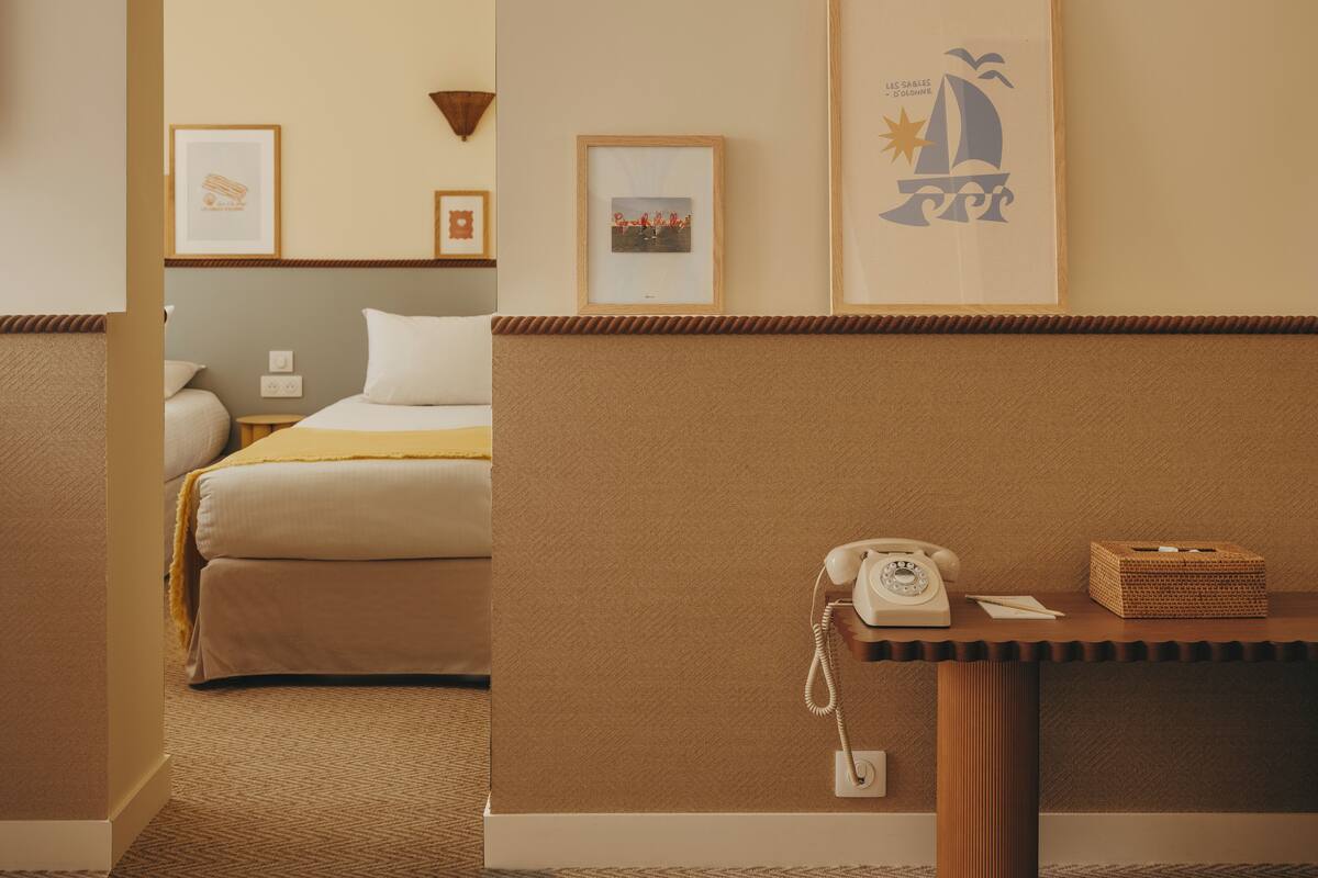 A hotel room with a bed, bedside table with a telephone, and framed pictures on the wall.