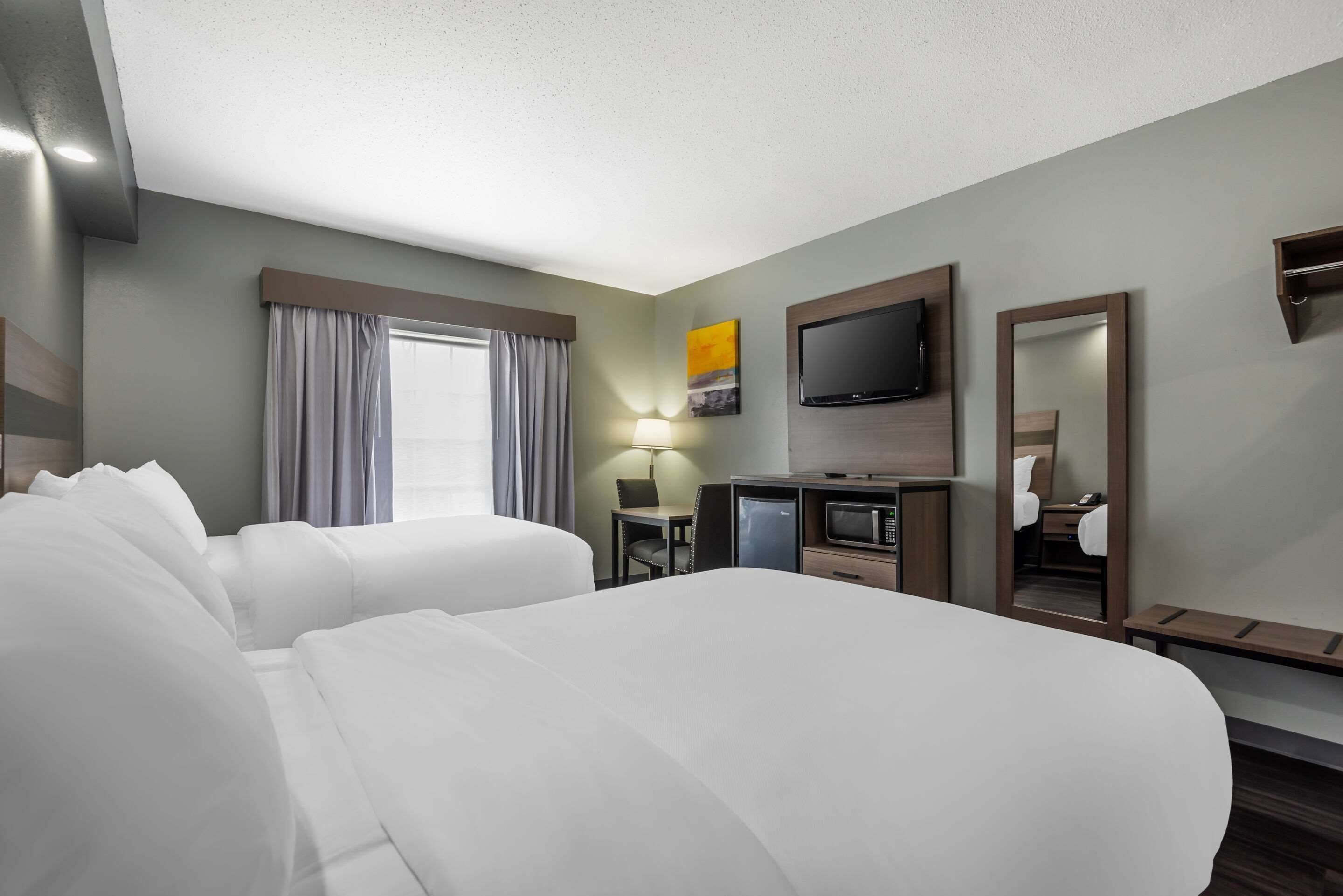 A hotel room with two beds, a desk with a computer, a TV, and a mirror.