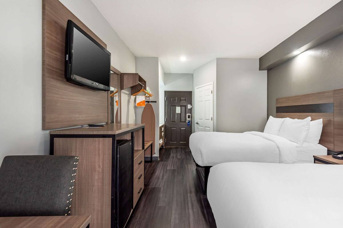 Habitación de hotel con televisión montada en la pared, escritorio con silla, dos camas y un armario.