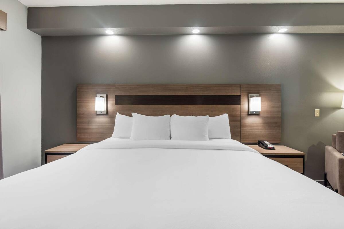 Habitación de hotel con una cama grande, dos mesitas de noche, un cabecero de madera y dos lámparas de pared.