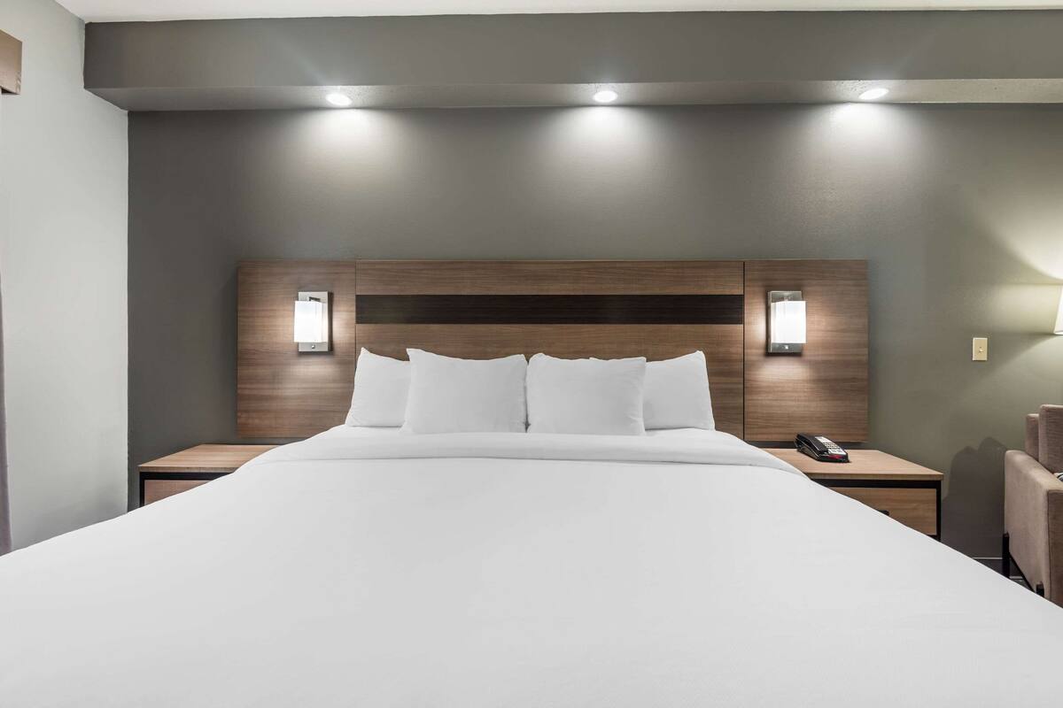Habitación de hotel con una cama grande, dos mesitas de noche, un cabecero de madera y dos lámparas fijadas a la pared.