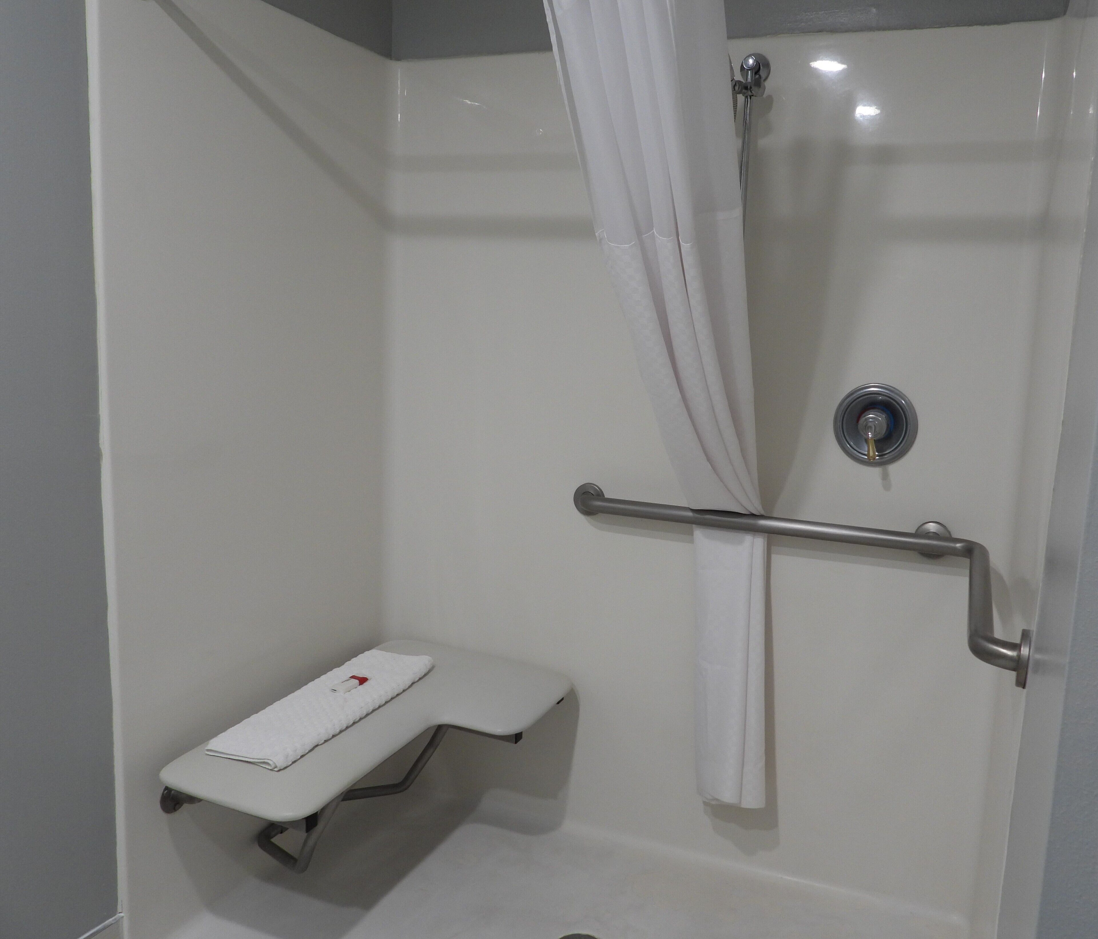 A shower with a grab bar, a white towel, and a small bench.