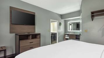 Una habitación de hotel moderna con una cama grande, un aparador de madera, un televisor de pantalla plana en la pared, un baño con espejo y una mesita pequeña.