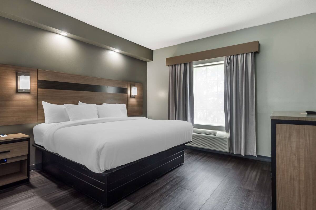 Una habitación de hotel moderna con una cama grande, una mesita de noche, un escritorio y una ventana con cortinas.