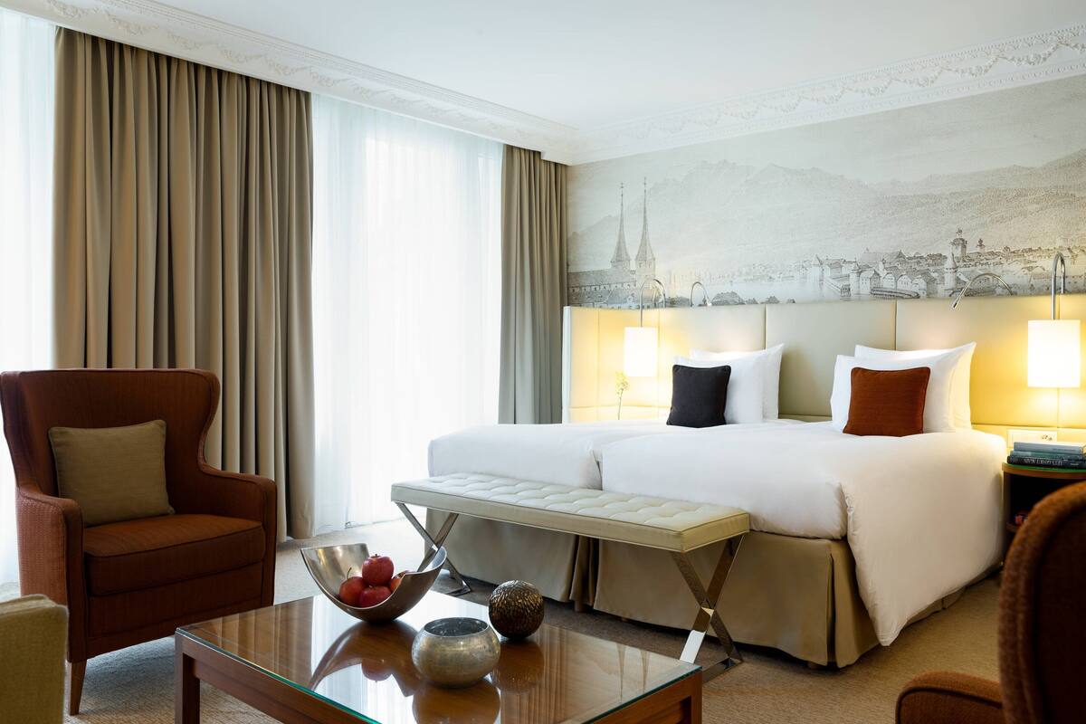 A hotel room with a large bed, a chair, a table with a bowl of fruit, and a mural on the wall.