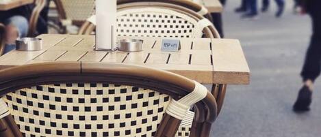 Mesas de mimbre al aire libre con posavasos metálicos, ubicadas en un área pública de estar.