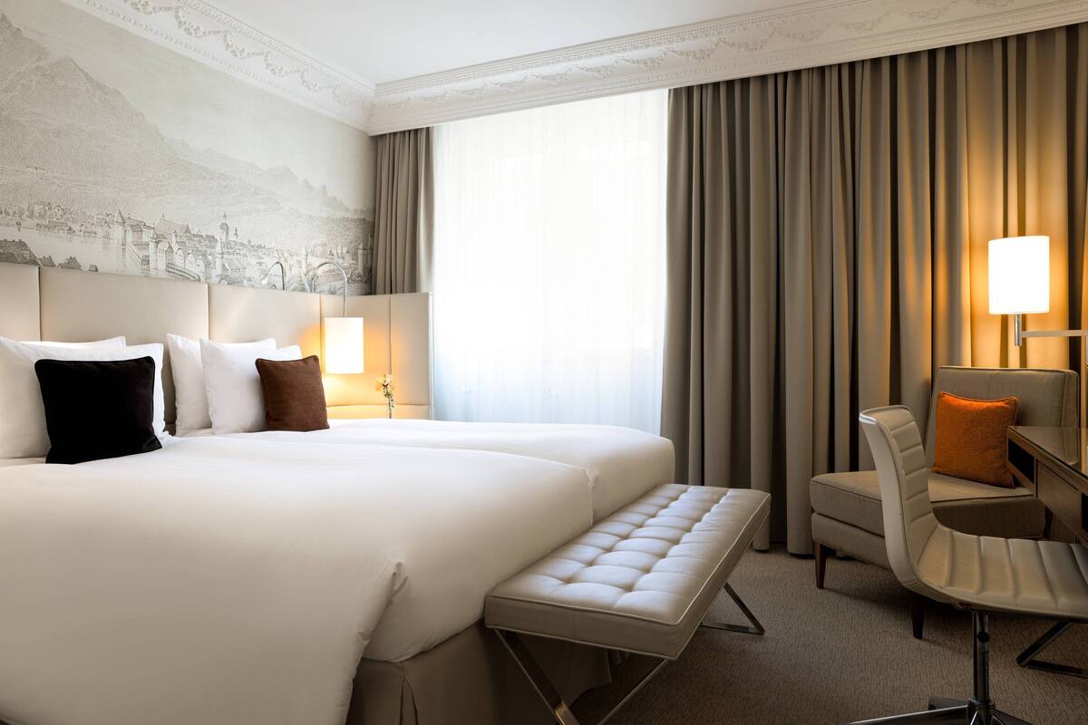 A hotel room with a large bed, a bench, a chair, and a desk.