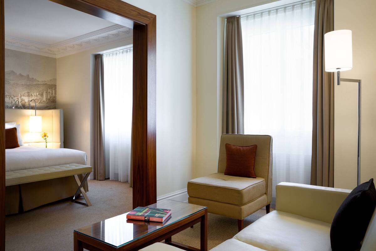 A hotel room with a bed, two armchairs, a coffee table, and a lamp.