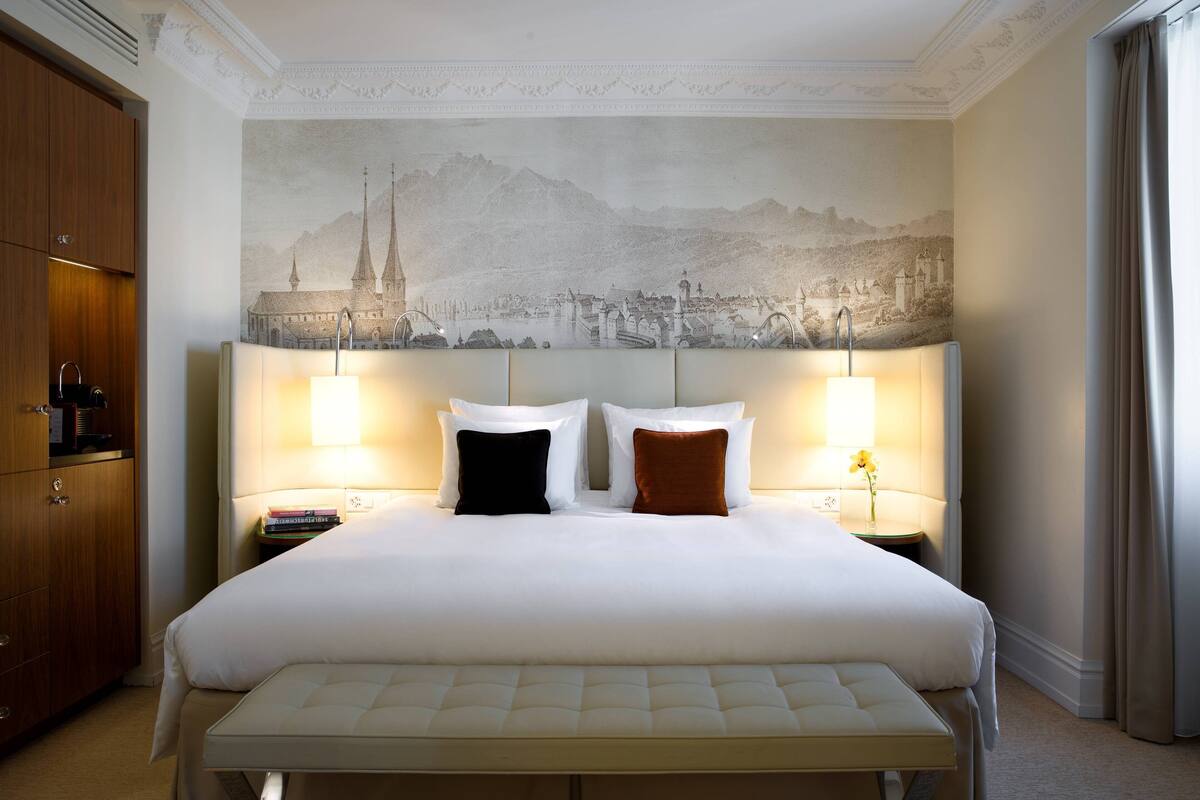 A hotel room with a large bed, two bedside lamps, a nightstand, and a wall mural.