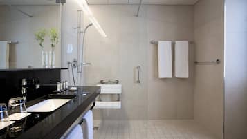 Un baño moderno con encimera negra, lavamanos blanco y zona de ducha con mampara de vidrio.