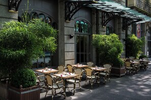 An outdoor cafe with wicker tables and chairs, surrounded by greenery and a stone building with arched windows. - Renaissance Lucerne Hotel (Lucerne)