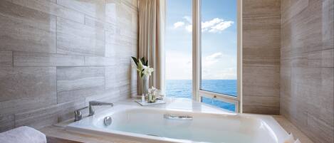 Un baño moderno con una bañera grande, una ventana con vistas al mar y un florero con flores en la encimera.