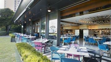 Un área de comedor al aire libre con mesas y sillas, una zona de bar con mostrador y vistas a la ciudad.