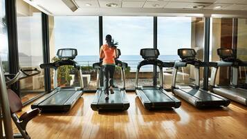 A gym with treadmills and a large window overlooking the ocean.