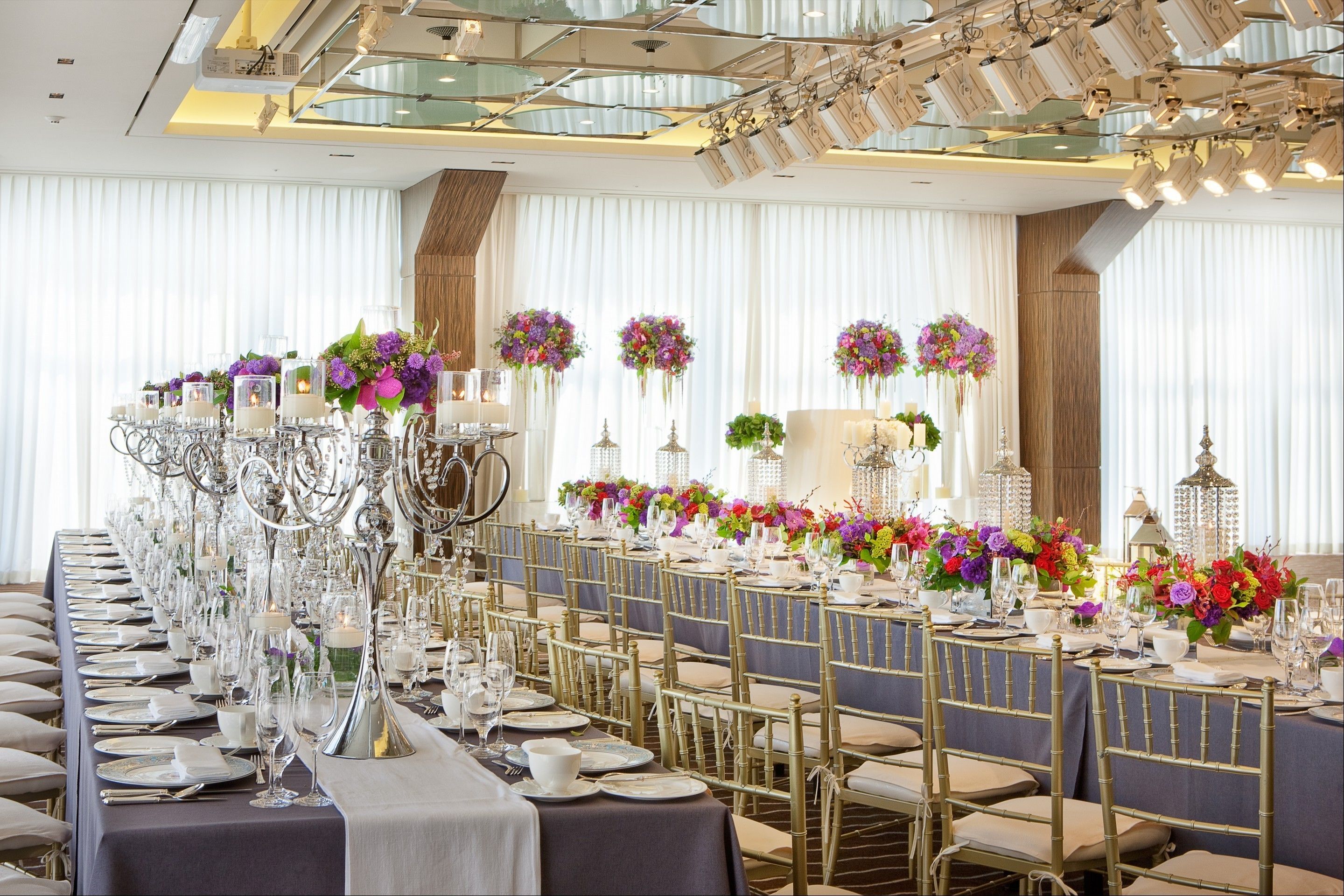 A long banquet table with gold chairs, white tablecloths, and floral centerpieces.