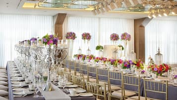 A long banquet table with gold chairs, white tablecloths, and floral centerpieces.