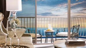 Un balcón con vista al mar, una mesa con jarrón y flores, y una silla.